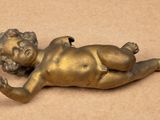 brass statue of a baby lying on its back on a brown surface