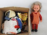 une poupée debout à côté d'un carton rempli de vêtements