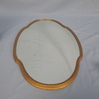miroir posé sur une table blanche, avec un cadre doré et un fond blanc