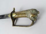 a gold colored sword with a black handle on a white surface