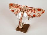 Sculpture de papillon en verre orange et blanc, posée sur un socle, sur fond blanc