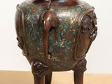 a bronze vase sitting on a wooden stand on a table