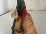 figurine of a woman sitting on a sack with a hat on her head