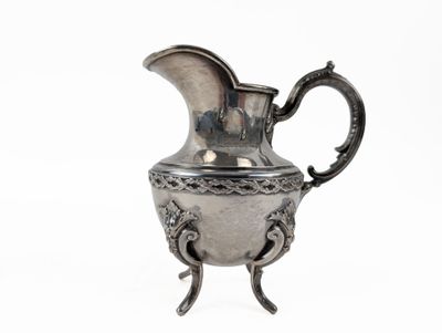 a silver pitcher that is on a stand on a white surface