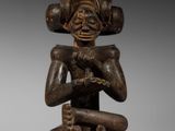 une image représentant une statue en bois d'une personne assise sur un tabouret