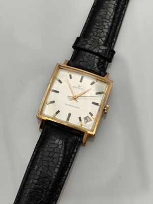 gros plan d'une montre sur une surface blanche avec un bracelet noir