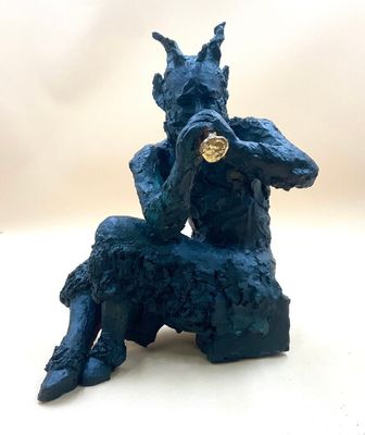 statue of a man sitting on a rock with a gold coin in his mouth