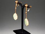 a pair of jade and gold earrings on a black stand