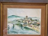 framed watercolor painting of a village by a river in a gold frame