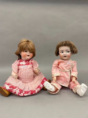 deux petites poupées assises l'une à côté de l'autre sur une surface grise