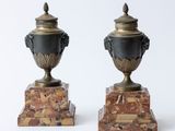 pair of black and gold urns on marble bases on a white background