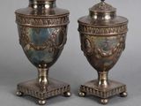 pair of antique silver plated urns on pedestals on grey background