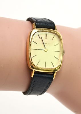 une montre en or avec un bracelet en cuir noir au poignet d'une femme