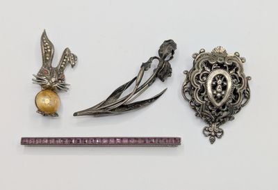 two silver brooches and a gold broocher are next to a ruler