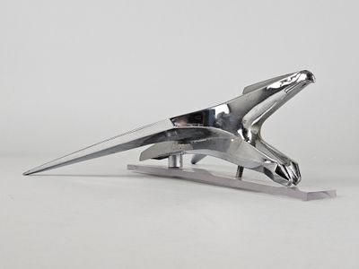 sculpture en métal argenté représentant un oiseau, posée sur un socle et disposée sur une surface blanche