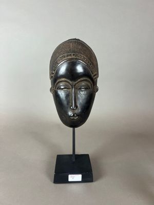 un masque en bronze posé sur un socle noir, avec un fond blanc