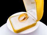 a gold wedding ring in a yellow box on a white plate