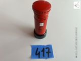 une boîte aux lettres rouge posée sur une surface blanche, à côté d'un morceau de papier bleu