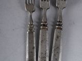 three forks and a knife on a table with a white background