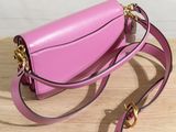 the small pink bag is sitting on a wooden table next to a white wall