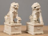 pair of white porcelain foo foo statues on pedestals on wooden table