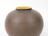 a brown vase with a yellow rim sitting on a white surface