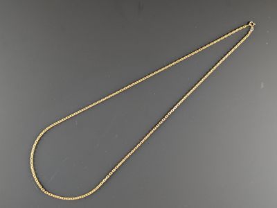un collier en or avec une chaîne posée sur une surface grise