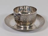 a silver cup and saucer sitting on a saucer