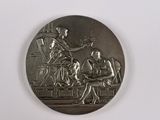 une photo représentant une médaille d'argent sur laquelle figurent une femme et un homme assis sur un banc