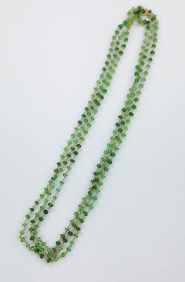 un gros plan d'un collier de perles vertes posé sur une surface blanche