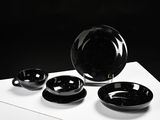 a black bowl and two black plates on a white table