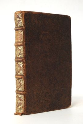 un vieux livre marron avec des bordures dorées posé sur une surface blanche