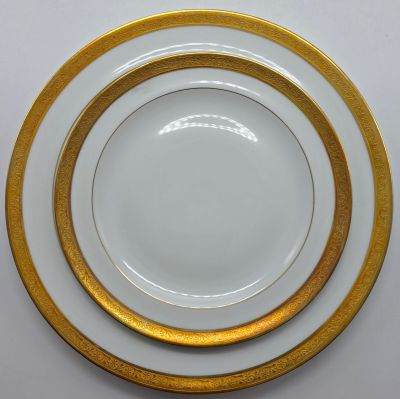 trois assiettes blanches et dorées, bordées d'or, posées sur une table blanche