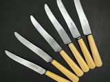 six couteaux sont alignés les uns à côté des autres sur une surface noire