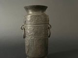 an old silver vase sitting on top of a table next to a gray wall