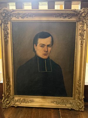 portrait d'un homme en manteau noir, dans un cadre doré, posé sur un plancher en bois