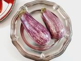 two eggplants sitting on a silver plate next to a bowl of tomatoes