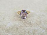 une photo d'une bague sertie d'une pierre violette posée sur une surface en marbre