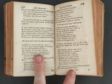 someone is holding a book open with a hand pointing at it