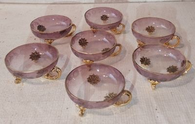 Six bols en verre violet aux bords dorés sont posés sur une table.
