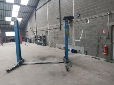 une photo d'un garage avec un pont élévateur bleu au milieu