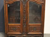 une armoire ancienne en bois, dotée de portes vitrées et ornée de sculptures sur les portes