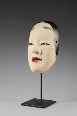 une image représentant un masque blanc posé sur un socle noir, sur fond gris