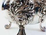 a silver tea pot on a stand on a white surface