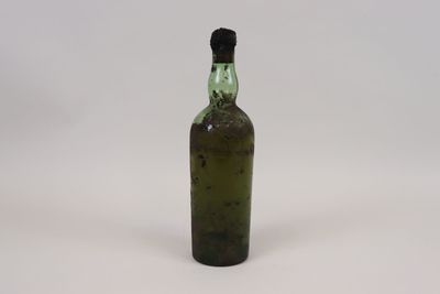 une vieille bouteille verte avec un bouchon noir posée sur une surface blanche