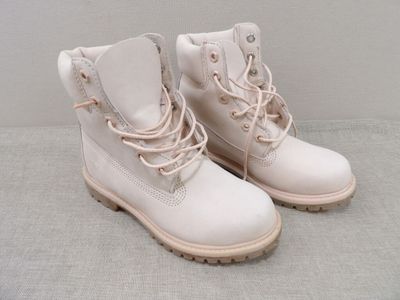 une paire de bottes blanches ornées de lacets roses, posées sur une surface grise