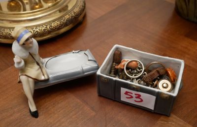 une figurine représentant une femme assise sur un lit, à côté d'une boîte contenant divers objets