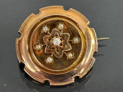 une broche en or ornée de perles, posée sur un fond noir