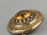 an image of a gold broochle with a citrine stone in the center