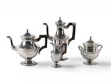 three silver teapots and two silver cups on a white surface